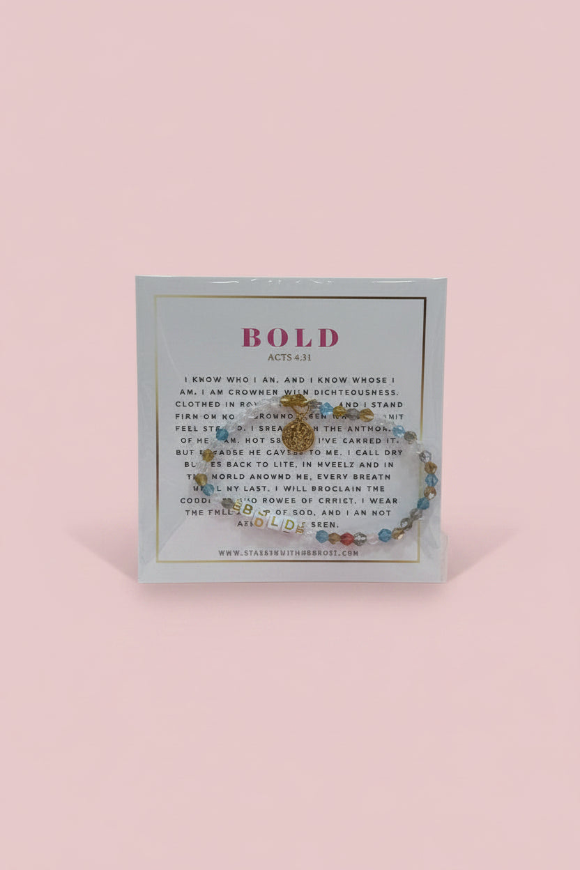 A hand holds a display card featuring a beaded bracelet with a gold-toned circular charm. The card has the word 'BOLD' printed at the top and a small brand name at the bottom.