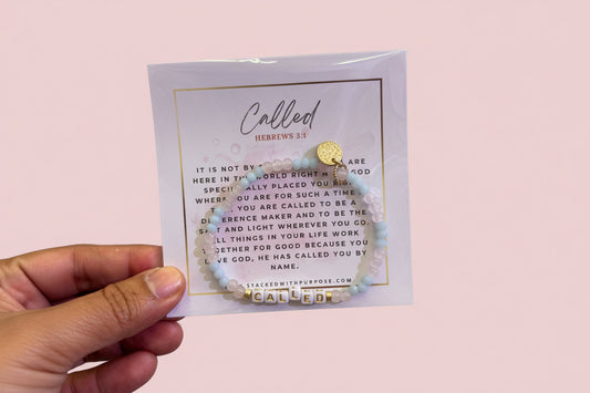 Hand holding a card with a necklace and 'Called' text on a pink background