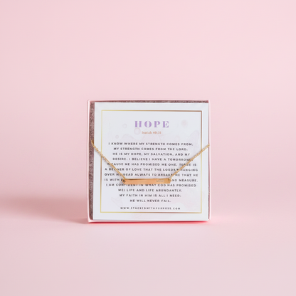 A gold bar chain bracelet displayed in a pink box with the word 'HOPE' written on it, against a white background.