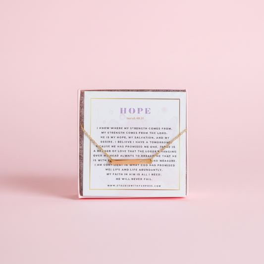 A gold bar chain bracelet displayed in a pink box with the word 'HOPE' written on it, against a white background.